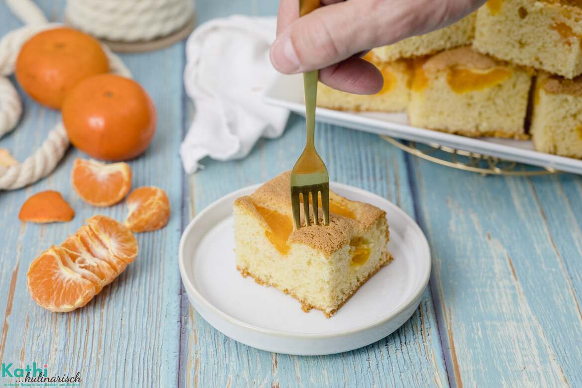 Jemand sticht mit einer goldenen Gabel in Stück Buttermilchkuchen mit Mandarinen.