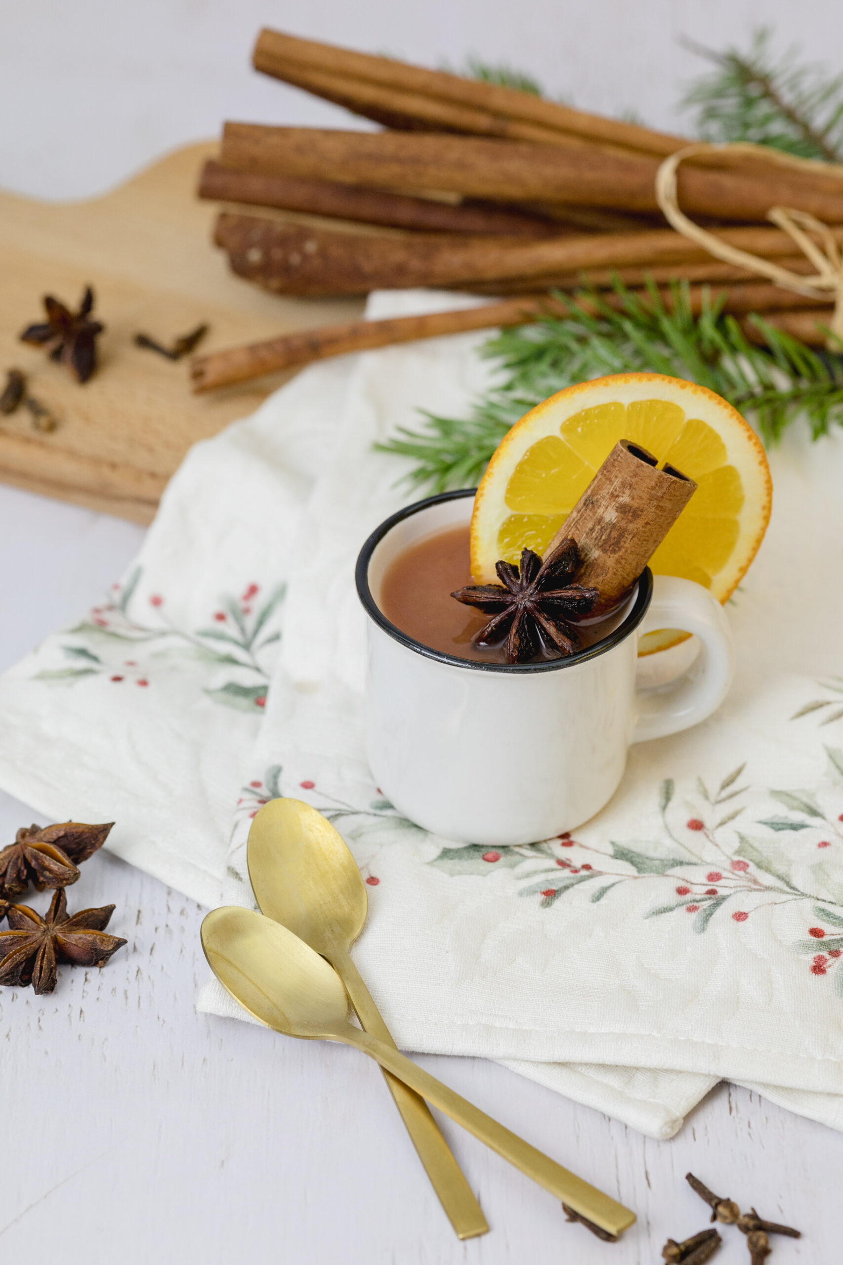 Eine Tasse mit Kinderpunsch steht am Tisch. Im Hintergrund sind Zimtstangen und Tannenzweige zu sehen. Sternanis und Gewürznelken runden das Bild ab.