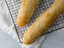 Zwei Stücke schnelle Baguette mit Trockenhefe liegen auf einem schwarzen Abkühlgitter. Darunter ist ein weißes Tuch zu sehen.