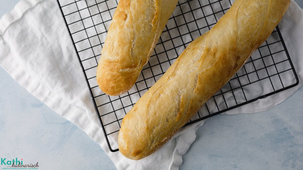 Zwei Stücke schnelle Baguette mit Trockenhefe liegen auf einem schwarzen Abkühlgitter. Darunter ist ein weißes Tuch zu sehen.